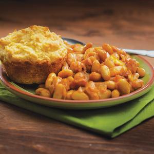 Photo of BBQ bakes beans and citrus-corn muffin on a plate with a green napkin beneath
