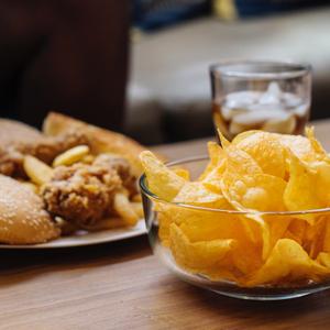 Photo of a bowl of potato chips, a glass of soda, and a fried chicken plate