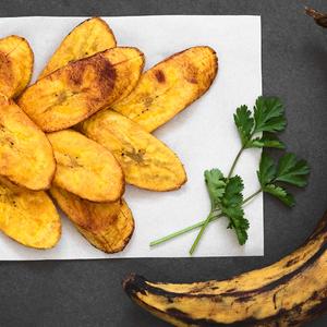Photo of baked plantains on a plate next to a whole, ripe plantain