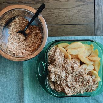 Photo of spiced topping being spooned over cooked apples in the baking dish