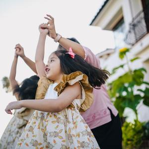 Photo of two young girls twirling with a parent, in front of a house and garden