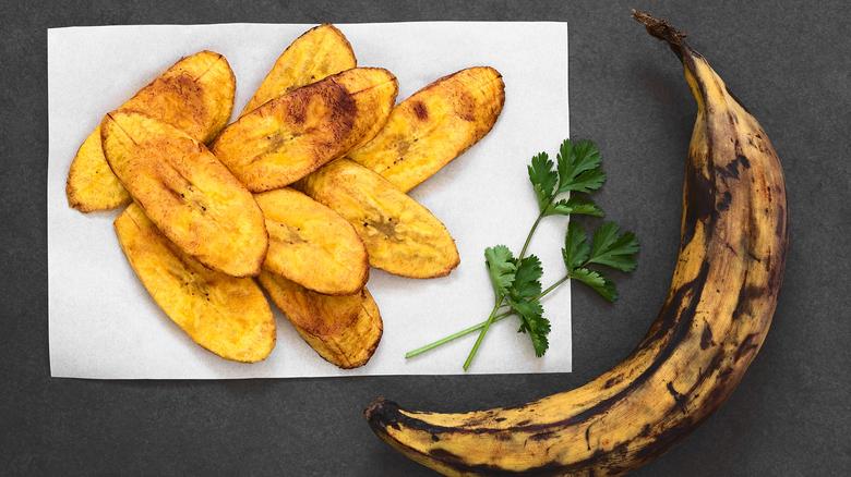 Photo of baked plantains on a plate next to a whole, ripe plantain