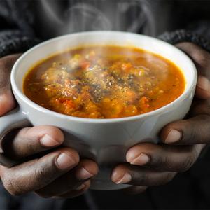Photo of a person holding a bowl of soup with steam coming up