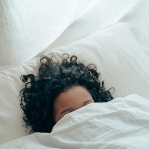 Photo of a person's head peaking out from under blankets, in a bed