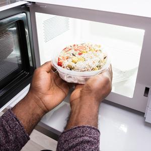 Photo of a person putting a meal into a microwave